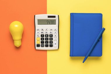 Bir ampul, bir hesap makinesi ve arka planda iki renkli bir defter. Elektrik ödemeleri kavramı.
