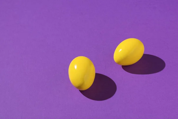 Two bright yellow eggs on a purple background. Creative photo of eggs.