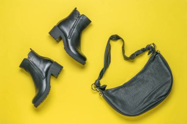 Bir çift siyah kadın ayak bileği botu ve sarı arka planda deri bir çanta. Modaya uygun deri şeyler. Düz yatıyordu.