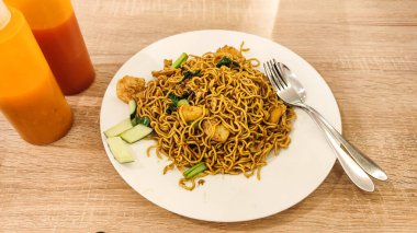 Yanında çatal ve kaşıkla servis edilen beyaz bir tabakta karides, sebze ve dilimlenmiş salatalıklı ramen tabağı. Asya mutfağı, lezzetli ve lezzetli yemek..