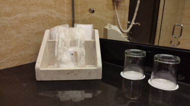 Temiz beyaz havlular, banyo tezgahındaki mendil kutusuyla birlikte bir tepside güzelce düzenlenir. Banyo içi modern ve minimalist..