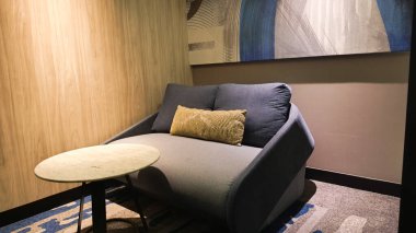 İçinde kavisli gri bir kanepe, kestane rengi bir aksanlı sandalye ve eşsiz geometrik sehpaların etrafına dizilmiş bej bir koltuk olan modern bir oturma odası.. 