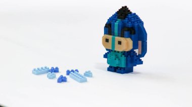 Plastik tuğlalardan yapılmış, beyaz arka planda minimalist tarzda izole edilmiş şirin mavi blok oyuncağı karakteri. Birbirine kenetlenmiş bloklardan inşa edilmiş küçük mavi pikselli biblo, temiz beyaz arka planda yaratıcı oyuncak tasarımı.