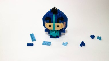 Plastik tuğlalardan yapılmış, beyaz arka planda minimalist tarzda izole edilmiş şirin mavi blok oyuncağı karakteri. Birbirine kenetlenmiş bloklardan inşa edilmiş küçük mavi pikselli biblo, temiz beyaz arka planda yaratıcı oyuncak tasarımı.