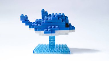 Plastik yapı taşlarından yapılmış mavi balina oyuncağı, küçük bir üste sergileniyor ve beyaz arka planda izole ediliyor. Birbirine kenetlenmiş tuğlalarla yapılmış şirin mavi balina heykelciği, temiz beyaz arka planda minimalist oyuncak tasarımı..