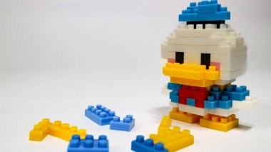Beyaz arka planda renkli plastik yapboz yapı taşlarından yapılmış şirin bir çizgi film ördek figürü. Minimalist bir stüdyo kompozisyonu olan yapı taşlarıyla yapılmış oyuncak bir ördek modeli..