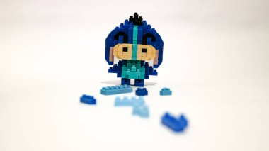 Plastik tuğlalardan yapılmış, beyaz arka planda minimalist tarzda izole edilmiş şirin mavi blok oyuncağı karakteri. Birbirine kenetlenmiş bloklardan inşa edilmiş küçük mavi pikselli biblo, temiz beyaz arka planda yaratıcı oyuncak tasarımı.