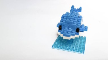 Plastik yapı taşlarından yapılmış mavi balina oyuncağı, küçük bir üste sergileniyor ve beyaz arka planda izole ediliyor. Birbirine kenetlenmiş tuğlalarla yapılmış şirin mavi balina heykelciği, temiz beyaz arka planda minimalist oyuncak tasarımı..