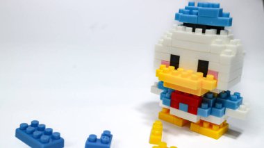 Beyaz arka planda renkli plastik yapboz yapı taşlarından yapılmış şirin bir çizgi film ördek figürü. Minimalist bir stüdyo kompozisyonu olan yapı taşlarıyla yapılmış oyuncak bir ördek modeli..