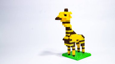 Beyaz arka planda renkli plastik yapı taşlarından yapılmış bir zürafa figürü. Yapı taşlarından yapılmış oyuncak bir zürafa modeli. Minimalist bir stüdyo resmi. Blok tarzı zürafa, beyaz bir yüzeye dağılmış parçalarla küçük bir üste duruyor..