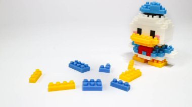 Beyaz arka planda renkli plastik yapboz yapı taşlarından yapılmış şirin bir çizgi film ördek figürü. Minimalist bir stüdyo kompozisyonu olan yapı taşlarıyla yapılmış oyuncak bir ördek modeli..