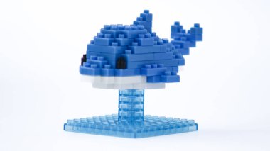 Plastik yapı taşlarından yapılmış mavi balina oyuncağı, küçük bir üste sergileniyor ve beyaz arka planda izole ediliyor. Birbirine kenetlenmiş tuğlalarla yapılmış şirin mavi balina heykelciği, temiz beyaz arka planda minimalist oyuncak tasarımı..