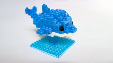 Plastik yapı taşlarından yapılmış mavi balina oyuncağı, küçük bir üste sergileniyor ve beyaz arka planda izole ediliyor. Birbirine kenetlenmiş tuğlalarla yapılmış şirin mavi balina heykelciği, temiz beyaz arka planda minimalist oyuncak tasarımı..