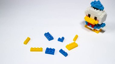 Beyaz arka planda renkli plastik yapboz yapı taşlarından yapılmış şirin bir çizgi film ördek figürü. Minimalist bir stüdyo kompozisyonu olan yapı taşlarıyla yapılmış oyuncak bir ördek modeli..