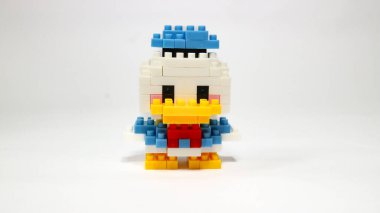 Beyaz arka planda renkli plastik yapboz yapı taşlarından yapılmış şirin bir çizgi film ördek figürü. Minimalist bir stüdyo kompozisyonu olan yapı taşlarıyla yapılmış oyuncak bir ördek modeli..