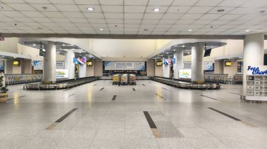 Havaalanı bagaj vagonları, renkli reklam panelleri ve büyük cam pencerelerden gelen doğal ışığı gösteren parlak ışıklı terminal koridorlarını hizaya sokuyor..