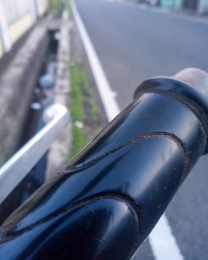 Bulanık asfalt yol arka planına sahip parlak siyah bir motorsiklet gidonunun ayrıntılı makro dokusu.