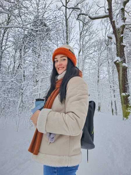 Gülümseyen kadın ormanda karlı kış yürüyüşünün tadını çıkarıyor.