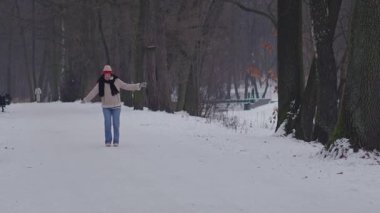 Kış parkında karlı bir yolda ağır çekimde koşan mutlu genç kadın.