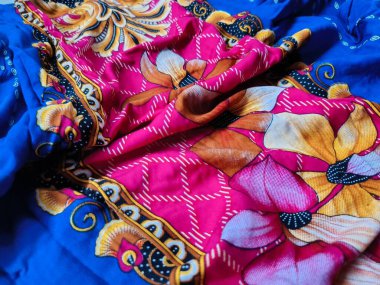 Batik kumaşın arka planı ve deseni baskın mavi ve kırmızı renklerle çiçekleri betimler.