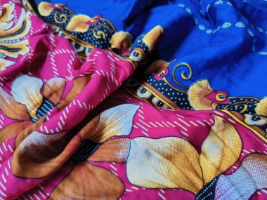 Batik kumaşın arka planı ve deseni baskın mavi ve kırmızı renklerle çiçekleri betimler.