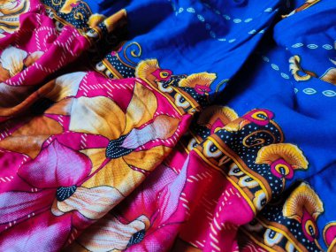 Batik kumaşın arka planı ve deseni baskın mavi ve kırmızı renklerle çiçekleri betimler.