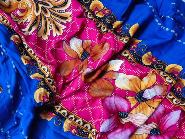 Batik kumaşın arka planı ve deseni baskın mavi ve kırmızı renklerle çiçekleri betimler.