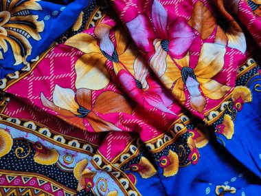 Batik kumaşın arka planı ve deseni baskın mavi ve kırmızı renklerle çiçekleri betimler.