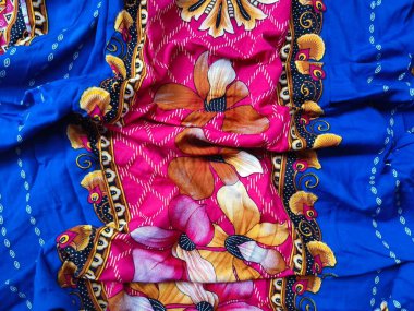 Batik kumaşın arka planı ve deseni baskın mavi ve kırmızı renklerle çiçekleri betimler.