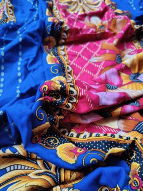 Batik kumaşın arka planı ve deseni baskın mavi ve kırmızı renklerle çiçekleri betimler.