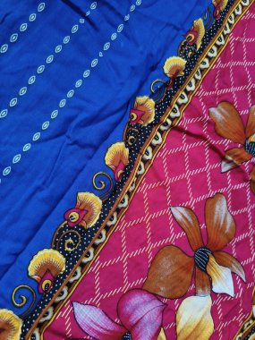 Batik kumaşın arka planı ve deseni baskın mavi ve kırmızı renklerle çiçekleri betimler.