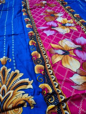 Batik kumaşın arka planı ve deseni baskın mavi ve kırmızı renklerle çiçekleri betimler.