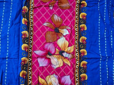 Batik kumaşın arka planı ve deseni baskın mavi ve kırmızı renklerle çiçekleri betimler.