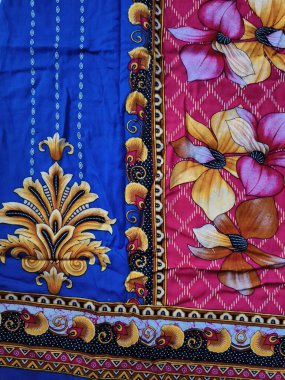 Batik kumaşın arka planı ve deseni baskın mavi ve kırmızı renklerle çiçekleri betimler.