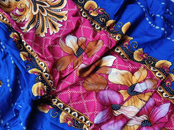 Batik kumaşın arka planı ve deseni baskın mavi ve kırmızı renklerle çiçekleri betimler.