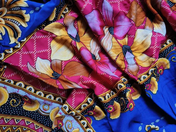 Batik kumaşın arka planı ve deseni baskın mavi ve kırmızı renklerle çiçekleri betimler.