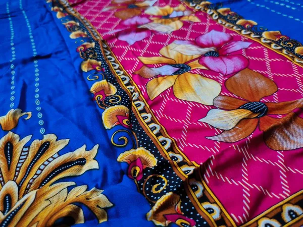 Batik kumaşın arka planı ve deseni baskın mavi ve kırmızı renklerle çiçekleri betimler.