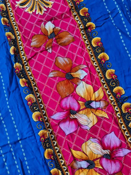 Batik kumaşın arka planı ve deseni baskın mavi ve kırmızı renklerle çiçekleri betimler.