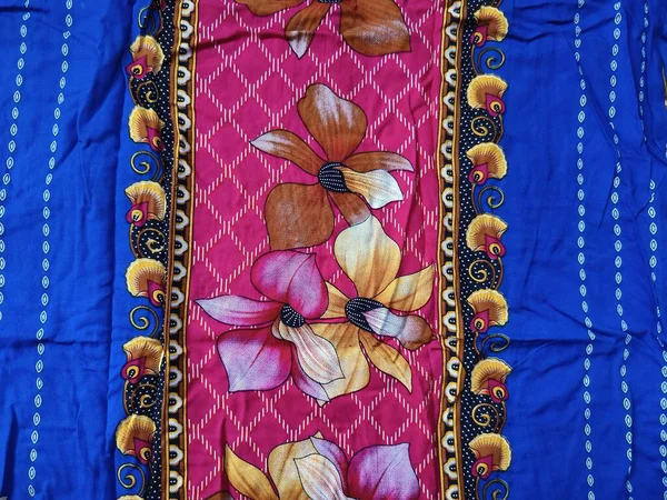Batik kumaşın arka planı ve deseni baskın mavi ve kırmızı renklerle çiçekleri betimler.