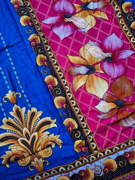 Batik kumaşın arka planı ve deseni baskın mavi ve kırmızı renklerle çiçekleri betimler.