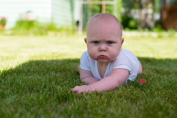 Ребенок лежит на траве в саду и хмурится — стоковое фото