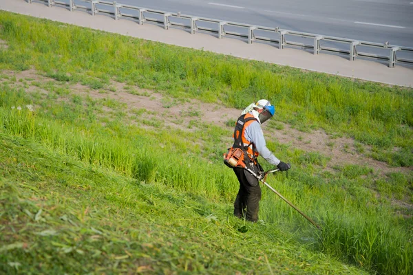 The worker in a uniform and mask cuts off a grass