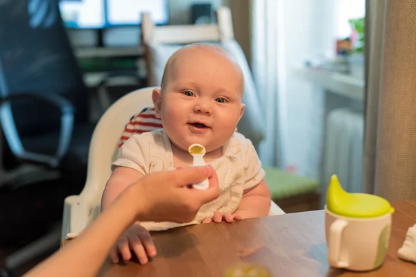 Niño se sienta en una silla, comiendo y riendo —  Fotos de Stock