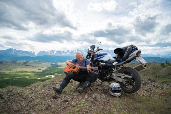 Glatzköpfiger Motorradfahrer spielt auf Motorrad sitzend Gitarre Stockbild