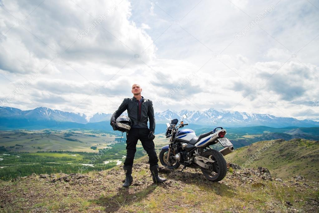 Bald rider stand on a mountain next to a motorcycle