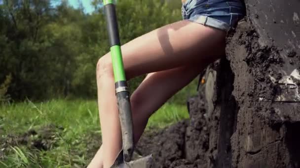 Chica con una pala en la tierra junto al coche atascado — Vídeos de Stock