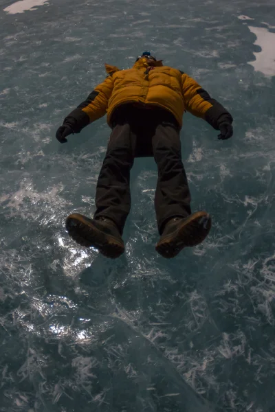 O homem de casaco amarelo deitado no gelo do Lago Baikal — Fotografia de Stock