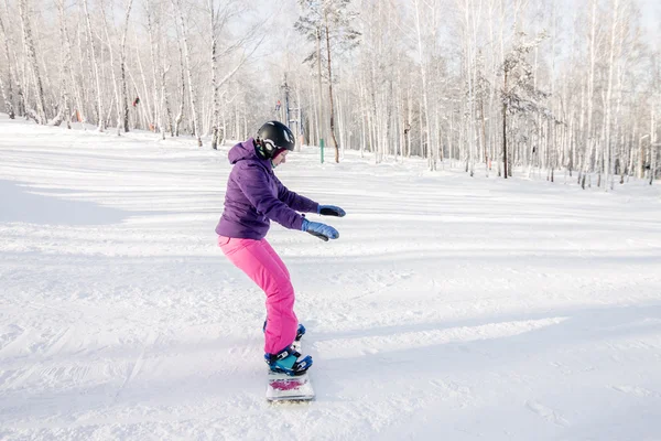 Menina em casaco roxo e calças rosa aprender passeio de snowboard — Fotografia de Stock