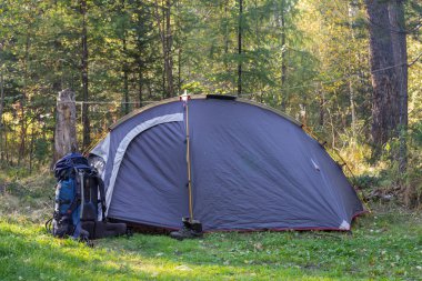Bir çadır ve gün batımında ormandaki botları bir sırt çantası