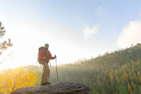 Man met rugzak en trekking pole in bandana staande op een roc — Stockfoto